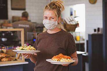 Waitress wearing face mask working in a cafe, carrying plates of food