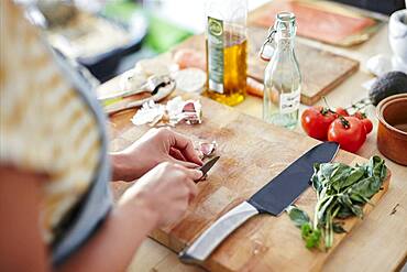 Woman in kitchen preparing garlic for cooking on chopping board