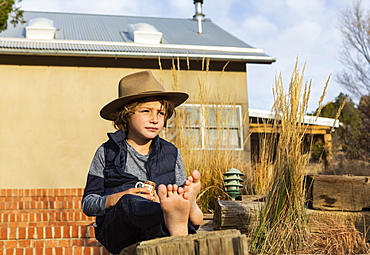 Portrait of young boy wearing fedora hat relaxing on his porch