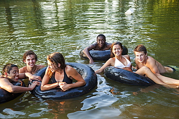 A group of young people, boys and girls, swimming and floating using swim floats and inflated tyres, Maryland, USA