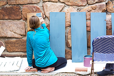 Teenage girl painting wooden shelves blue