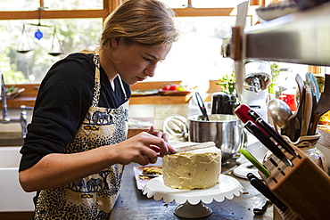 Teenage girl in kitchen applying icing to cake