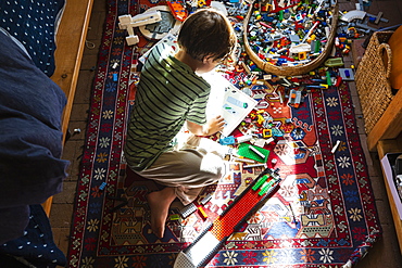 Boy sitting among toys on his bedroom floor in a patch of sunlight