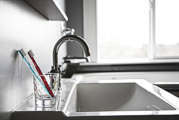 Toothbrushes in drinking glass in domestic bathroom