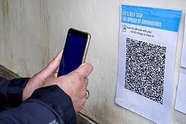 Close-up of person with smartphone scanning QR code in conjunction with the Covid-19 app.