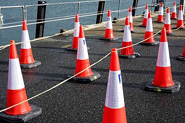 Close up of large number of traffic cones lined up on a harbour wall.