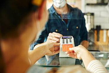 Woman wearing face mask holding contactless payment device, customer paying by mobile phone