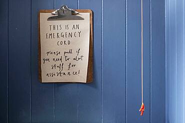 Close up of clipboard with emergency cord instructions on blue wall.