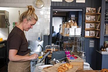 Waitress standing at counter in a cafe, working the till.