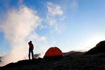 Woman standing by tent at sunrise, Iceland