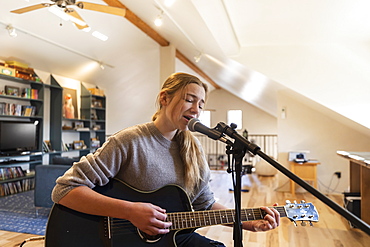 Fourteen year old teenage girl playing her guitar and singing at home in loft space