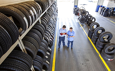 Two mechanics working the tire area of an auto repair shop, using a digital tablet