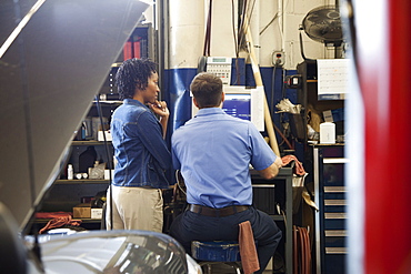 Mechanic and customer look at computer screen in auto repair shop