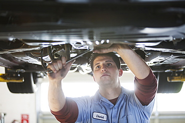 Mechanic in a repair shop works on the underside of a car up on a lift