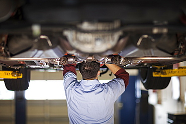 Mechanic in a repair shop works on the underside of a car up on a lift