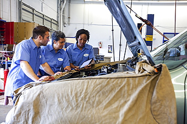 Three mechanics sharing a digital tablet and planning work on a car in for repair