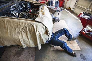 Mechanic lays on a trolley under a car in an auto repair shop