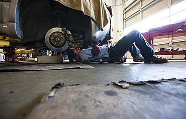 Mechanic lays on a trolley under a car in an auto repair shop