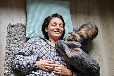 Woman lying on floor surrounded by two pet house rabbits shot from above, Bristol, United Kingdom