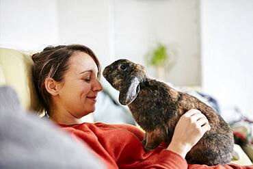 Pet house rabbit reaching towards woman with eyes closed on sofa, Bristol, United Kingdom