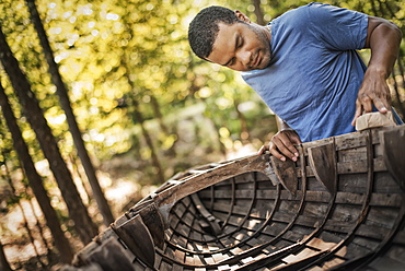 A young man repairing and sanding a traditional wooden rowing boat, New York state, USA