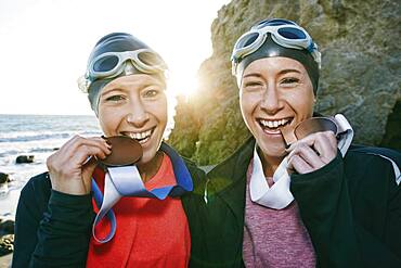 Two sisters, triathletes in swimhats and goggles wearing their large medals, winners.