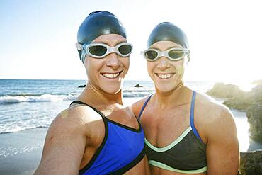 Two sisters, triathletes in training in swimwear, swimhats and goggles.