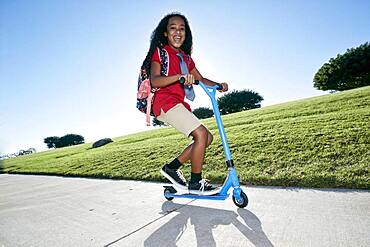 Young mixed race girl in pink shirt and formal tie, wearing a backpack on a scooter