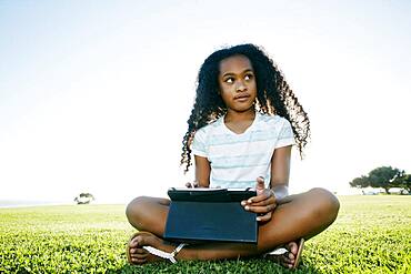 Nine year old mixed race girl outdoors with a digital tablet.