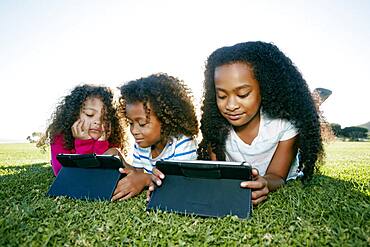 Young mixed race girl and her brother and sister with two digital tablets, screen time