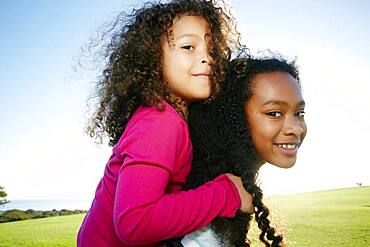 Young mixed race girl giving a younger sister a piggyback