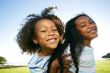 Young mixed race girl giving her younger brother a piggyback lift