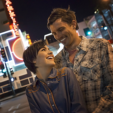 A couple, man and woman side by side in a city street at night. Neon signs, United States of America