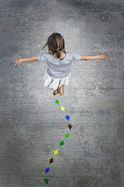 View from overhead of a child creating and walking along a line of coloured leaf shapes, Utah, USA