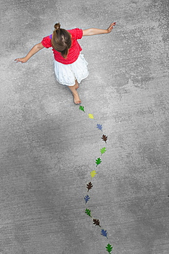 View from overhead of a child creating and walking along a line of coloured leaf shapes, Utah, USA