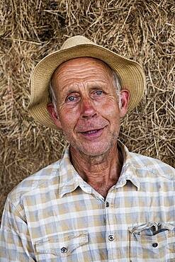 Farmer wearing checked shirt and sun hat, looking at camera.