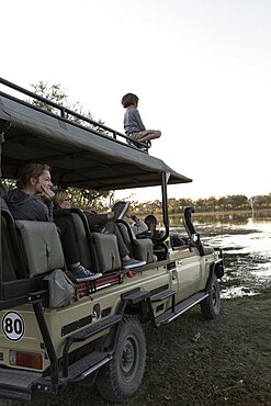 Eight year old boy on top of safari vehicle with passengers , Okavango Delta, Botswana