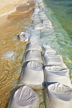 Sandbags in rows at the water's edge to prevent erosion of the beach