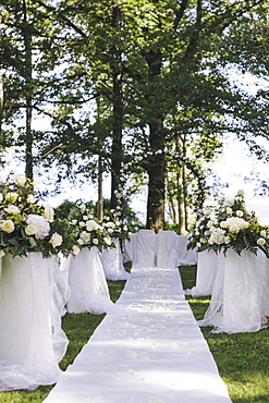 A garden with tables laid under the shade of tall trees, a floral arch, setting for a wedding, Lake Maggiore, Italy