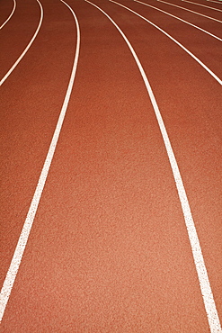 The surface of a sports athletics running track, red surface with white painted lane markings.