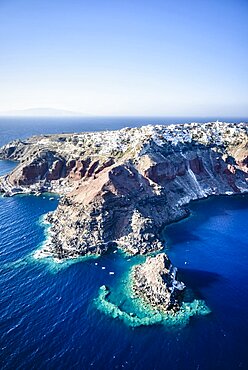 Aerial view of an island in the deep blue seas of the Aegean sea, rock formations, whitewashed houses perched on the cliffs.