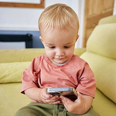 Toddler holding smart phone with animated expression indoors