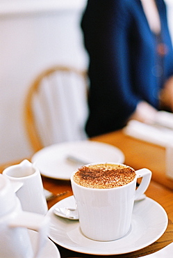 A woman seated at a table. A table setting and a large cup of coffee, England