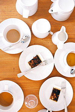 Overhead view of a table set with cups of tea, milk jugs and two slices of fruit cake on plates, England