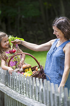 Mother and daughter standing in a garden with a basket of vegetables.