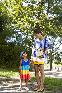 Mother and daughter standing outdoors, holding bird house, Kyoto, Honshu Island, Japan