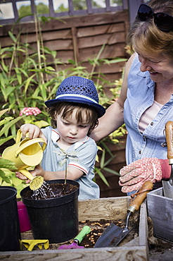 A woman and a young child water new seeds planted in a pot, England