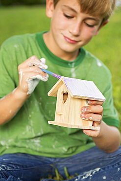 A boy in a garden, painting a bird houseAustin, Texas, USA