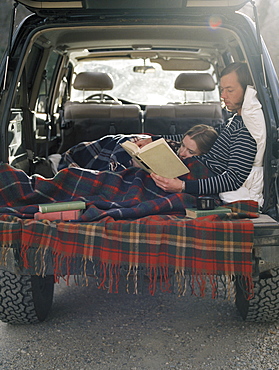 Young couple lying in the back of their car, reading a book, Millcreek, Utah, United States of America