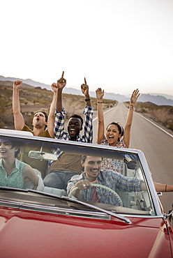 A group of friends in a red open top convertible classic car on a road trip, United States of America